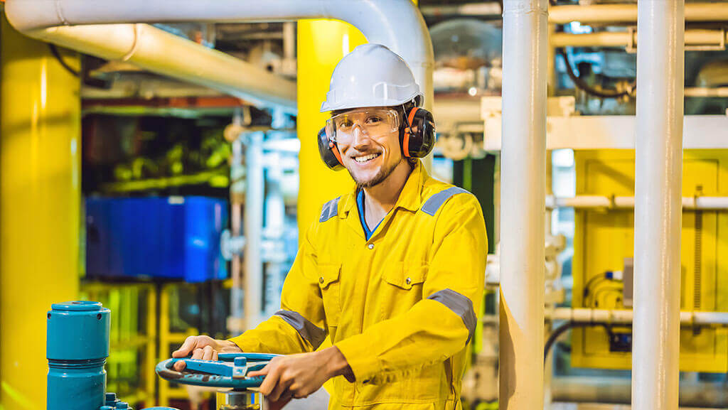 Young man in a yellow work uniform, glasses and helmet in industrial environment